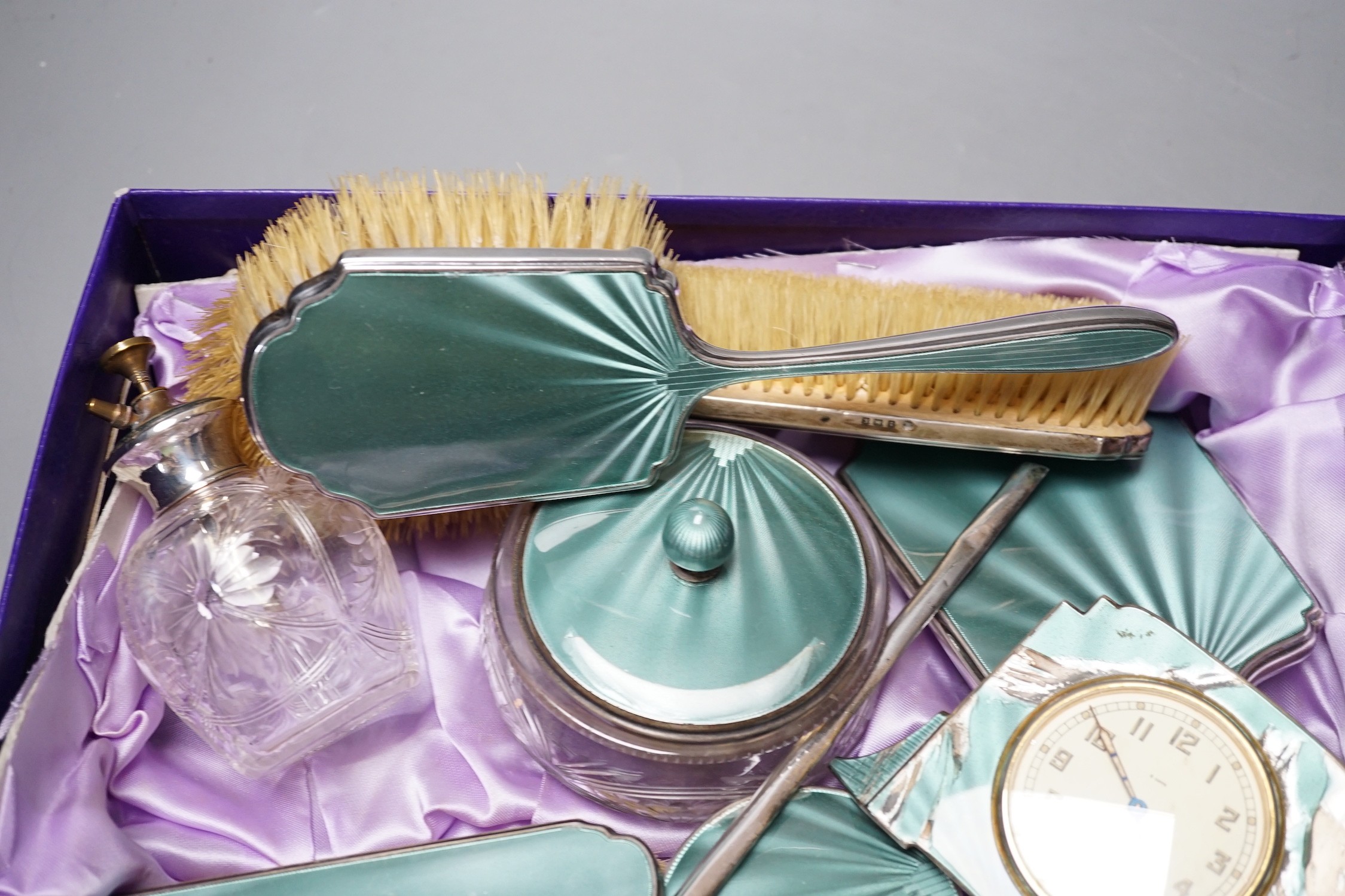 A George V silver and green guilloche enamel set nine piece dressing table set, by Albert Carter, Birmingham, 1933/4, together with a similar unmarked timepiece, comb teeth missing and enamel a.f.